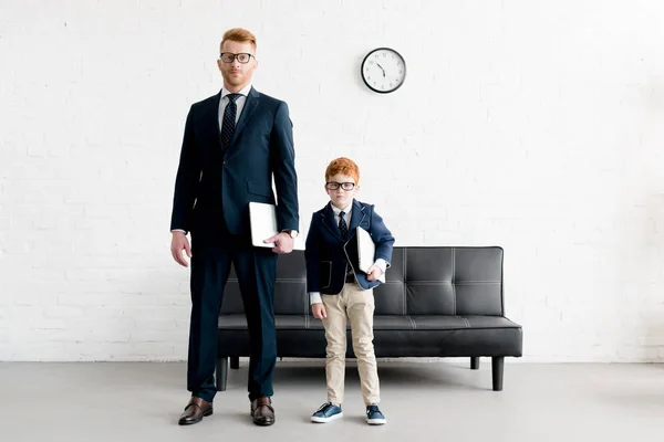 Sérieux adultes et pré-adolescents hommes d'affaires dans les lunettes tenant des ordinateurs portables et regardant la caméra — Photo de stock