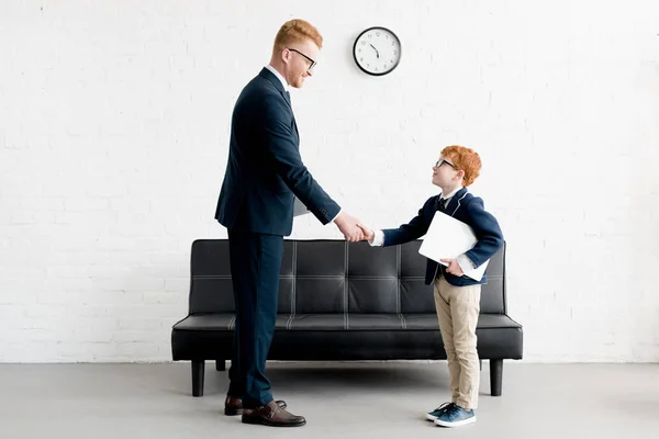 Vista lateral de adultos sonrientes y preadolescentes hombres de negocios estrechando la mano en la oficina - foto de stock