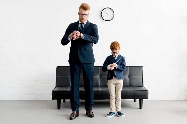 Vater und kleiner Sohn in offizieller Kleidung und Brille checken gemeinsam Armbanduhren — Stockfoto