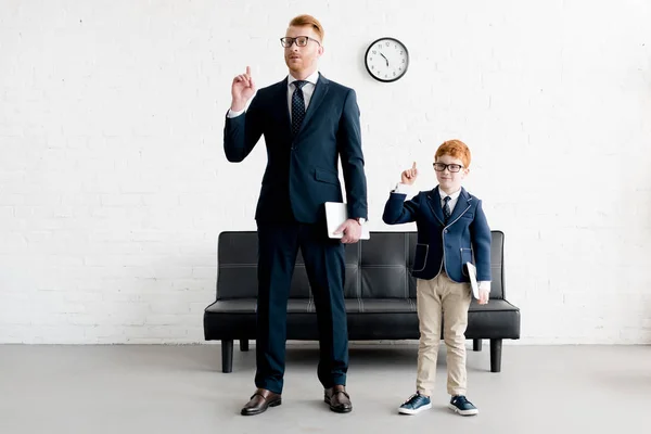 Father and little son businessmen holding digital tablets and pointing up with fingers — Stock Photo