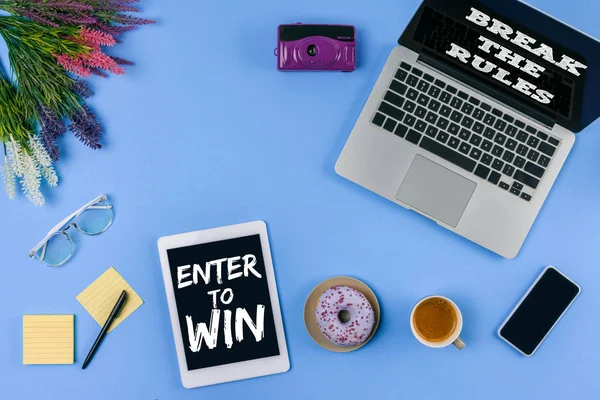 Top view of digital devices with inscriptions enter to win and break the rules, flowers, cup of coffee with doughnut and camera on blue — Stock Photo