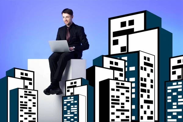 Smiling businessman with laptop sitting on white block between drawing buildings on blue — Stock Photo