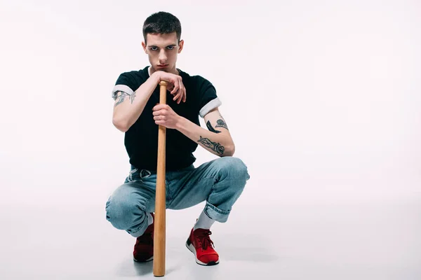 Young man sitting and leaning on baseball bat on white background — Stock Photo