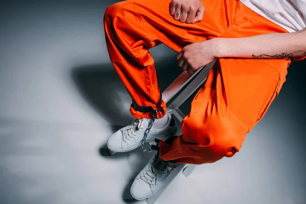 Top view of man in orange pants with cuffs on legs sitting on stool on dark background — Stock Photo