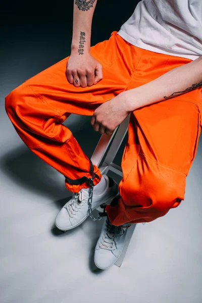 Вид зверху на людину у в'язничній формі з манжетами на ногах, що сидять на табуреті на темному фоні — стокове фото