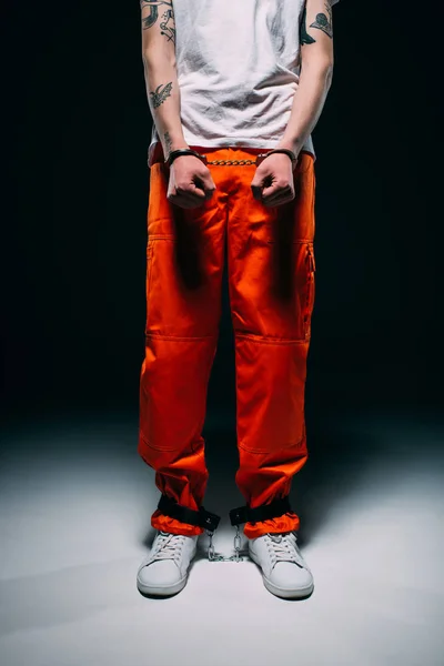 Cropped view of man wearing prison uniform with cuffs on dark background — Stock Photo
