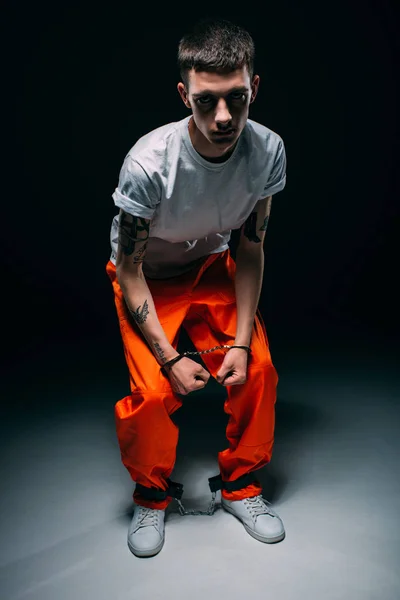 Sad male prisoner in orange uniform and cuffs on dark background — Stock Photo