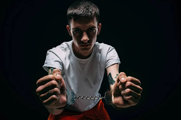 Sad man in prison uniform showing cuffs on dark background — Stock Photo