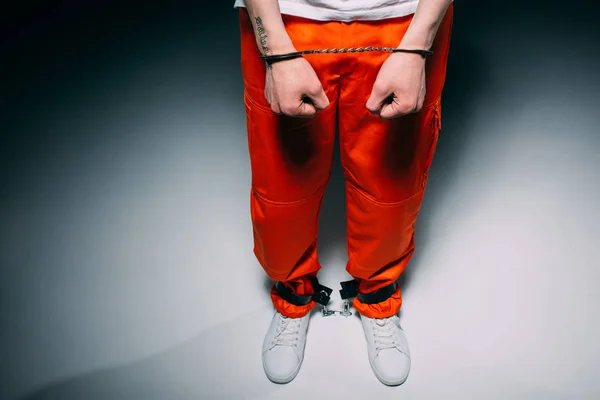 Vista recortada del hombre con pantalones naranja en puños sobre fondo oscuro - foto de stock
