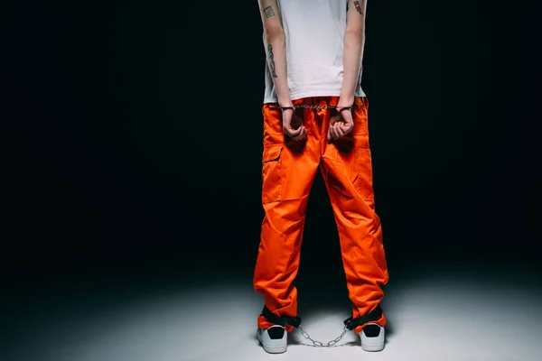 Cropped view of man wearing prison uniform with hands cuffed behind his back on dark background — Stock Photo