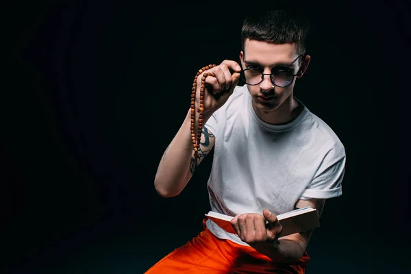 Male prisoner holding rosary and reading bible on dark background — Stock Photo