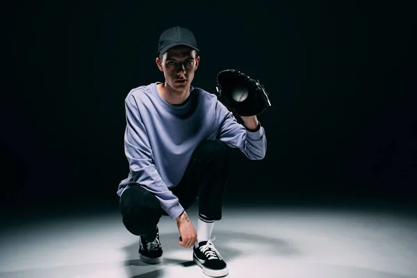 Schöner junger Mann mit Baseballhandschuhen, der Ball auf dunklem Hintergrund fängt — Stockfoto