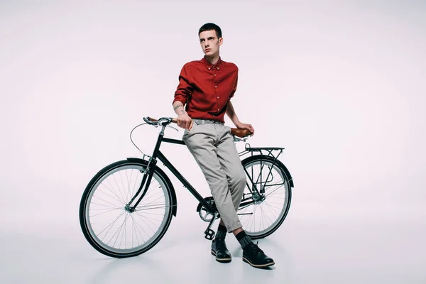 Молодий чоловік спирається на свій велосипед на білому тлі — стокове фото