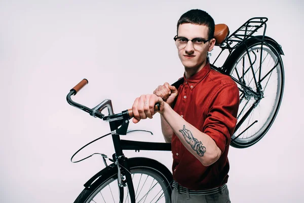 Young man in glasses holding his bicycle on shoulder isolated on white — Stock Photo
