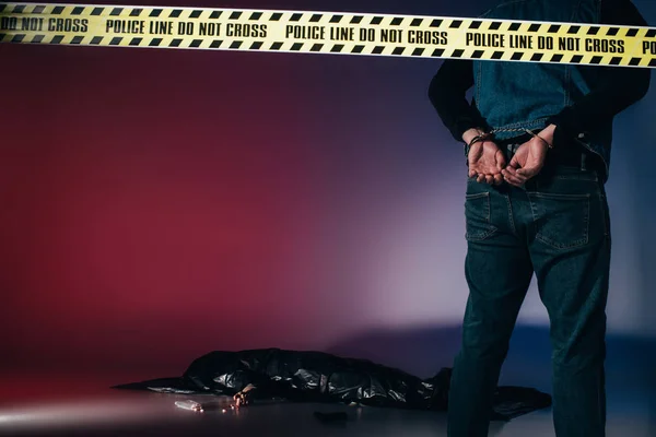 Vista trasera del asesino esposado detrás de la línea policial sobre fondo oscuro - foto de stock