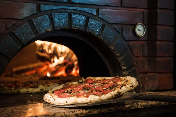 Vista de cerca del proceso de cocción de pizza cruda en estufa de madera en horno de ladrillo - foto de stock