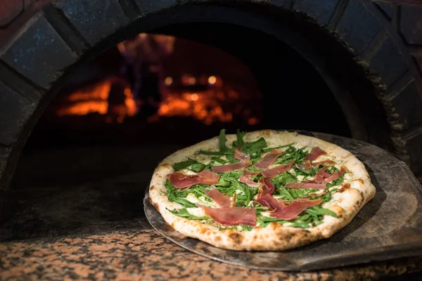 Vista de cerca del proceso de cocción de pizza cruda en estufa de madera en horno de ladrillo - foto de stock