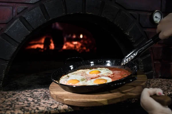 Colpo ritagliato di donna che mette le uova in padella nel forno di mattoni — Foto stock