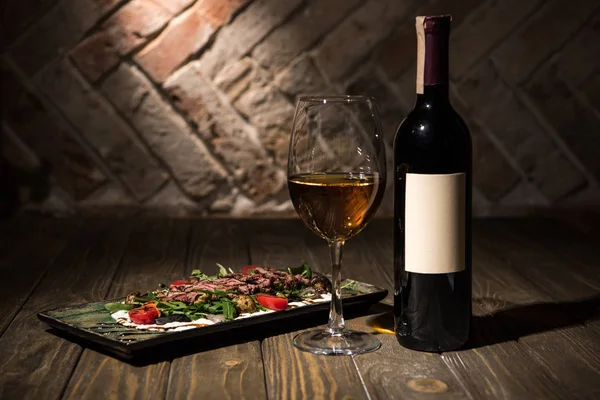 Vista de cerca de ensalada italiana con botella y copa de vino en la mesa de madera - foto de stock