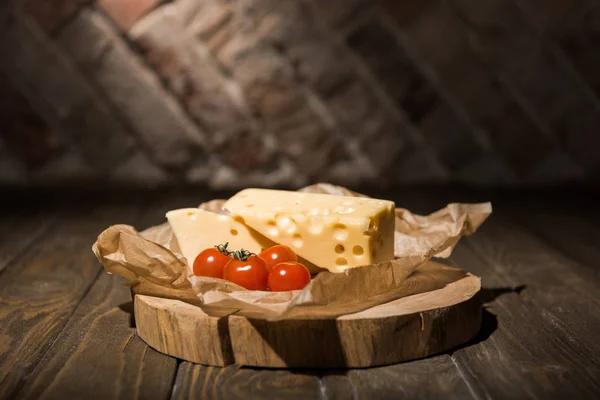 Close up view of fresh cherry tomatoes and cheese on baking paper on wooden stump — Stock Photo