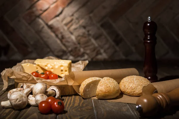 Close up view of fresh cherry tomatoes, cheese, mushrooms and loafs of bread on baking paper on wooden tabletop — Stock Photo