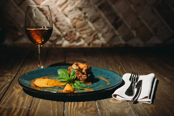 Vista de cerca del plato italiano con hojas de albahaca, copa de vino y cubiertos en la superficie de madera - foto de stock