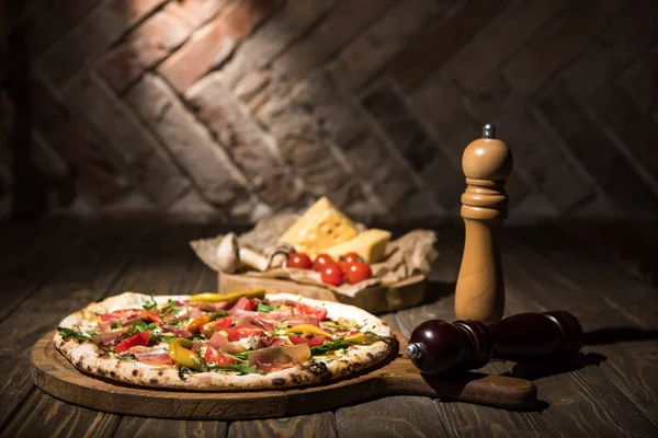 Selective focus of italian pizza, spices, cherry tomatoes and cheese on wooden tabletop — Stock Photo