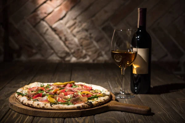 Enfoque selectivo de la pizza italiana, botella y copa de vino en la mesa de madera - foto de stock