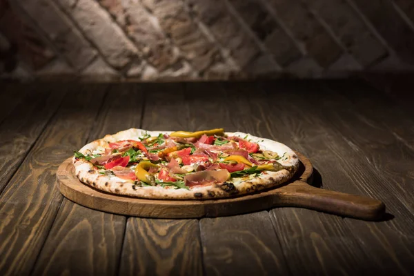 Close up view of italian pizza on cutting board on wooden tabletop — Stock Photo