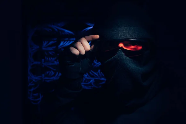 Obscured view of hacker in eyeglasses and mask looking at camera with cables on background — Stock Photo