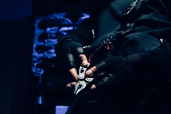 Cropped shot of hacker with nipping pliers in hands with cables on background — Stock Photo