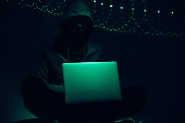 Imagen tonificada de silueta de hacker en sudadera con capucha usando el ordenador portátil - foto de stock
