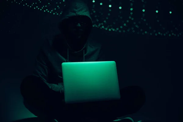 Toned picture of silhouette of hacker in hoodie using laptop — Stock Photo