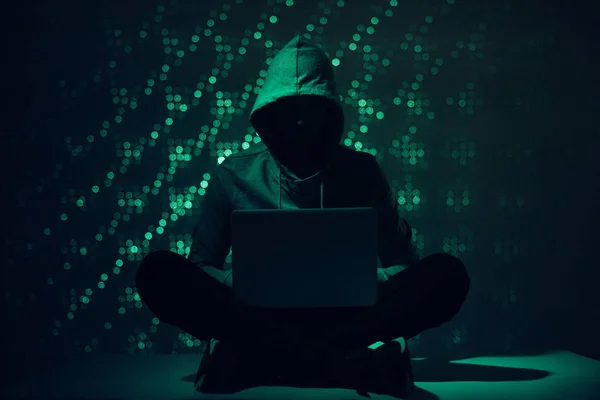 Тонированное изображение силуэта хакера в толстовке с помощью ноутбука — стоковое фото