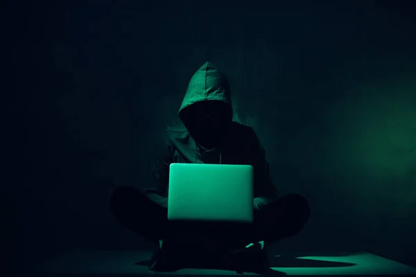 Тоновані зображення силует хакер в балахон, використовуючи ноутбук — стокове фото