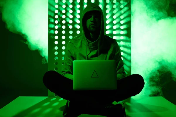 Imagen tonificada de hacker en sudadera con capucha con ordenador portátil y signo de triángulo en él - foto de stock