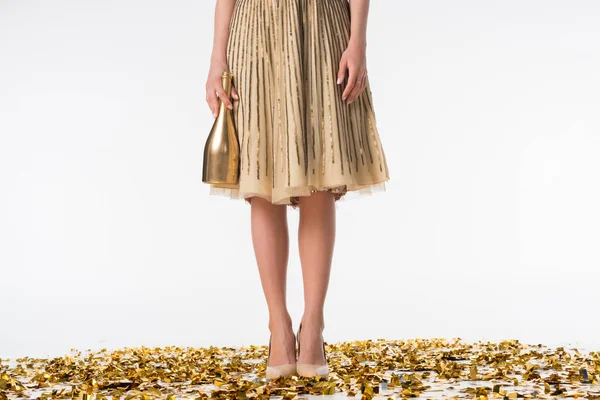 Imagen recortada de la mujer de pie sobre confeti en falda y la celebración de la botella de champán — Stock Photo