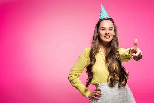 Mulher atraente com chapéu de festa mostrando polegar para cima isolado em rosa — Fotografia de Stock