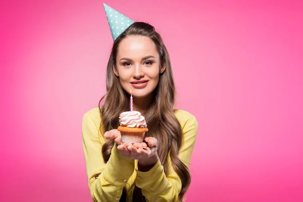 Jolie femme avec chapeau de fête tenant cupcake et regardant la caméra isolée sur rose — Photo de stock