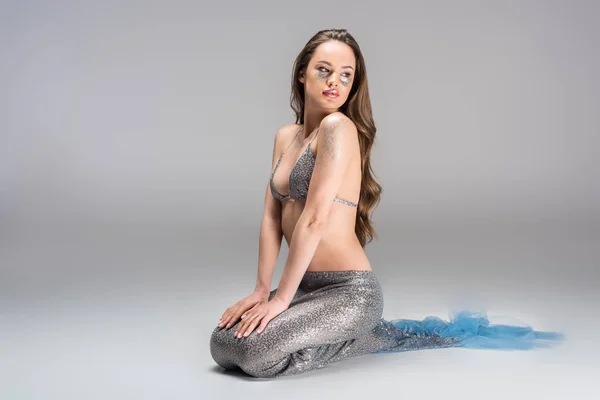 Attractive woman with mermaid tail and silver top sitting on floor — Stock Photo