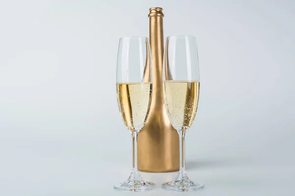 Golden bottle of champagne and transparent glasses on white surface — Stock Photo