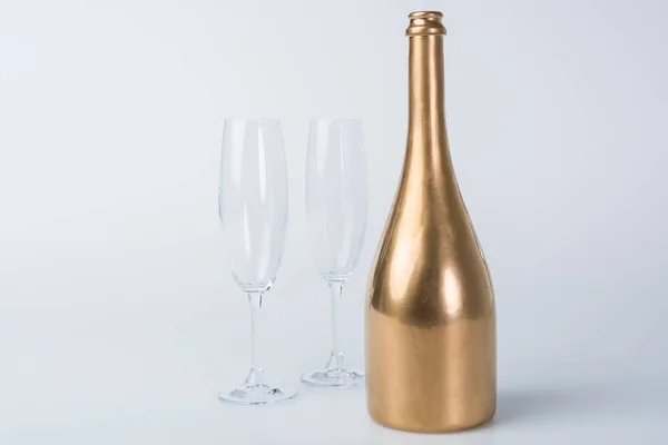 Bouteille de champagne dorée et verres vides sur surface blanche — Photo de stock