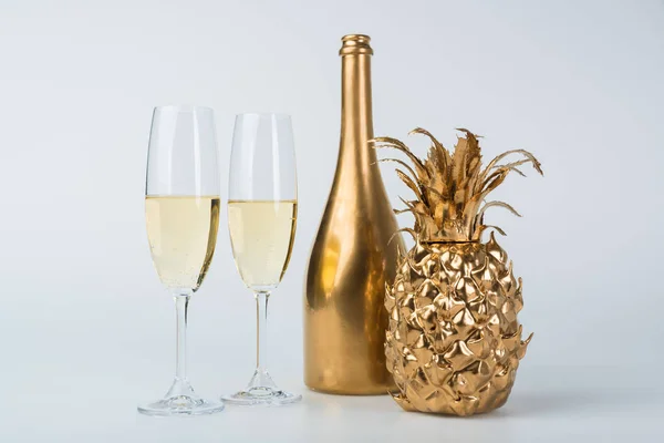 Bottiglia d'oro di champagne, ananas e bicchieri su superficie bianca — Foto stock