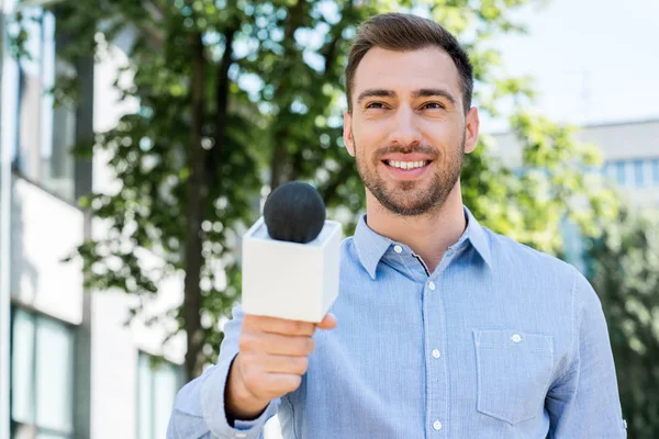 Улыбающийся журналист берёт интервью у микрофона — стоковое фото