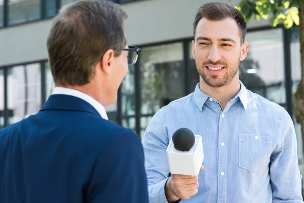 Periodista profesional entrevistando exitoso hombre de negocios con micrófono - foto de stock