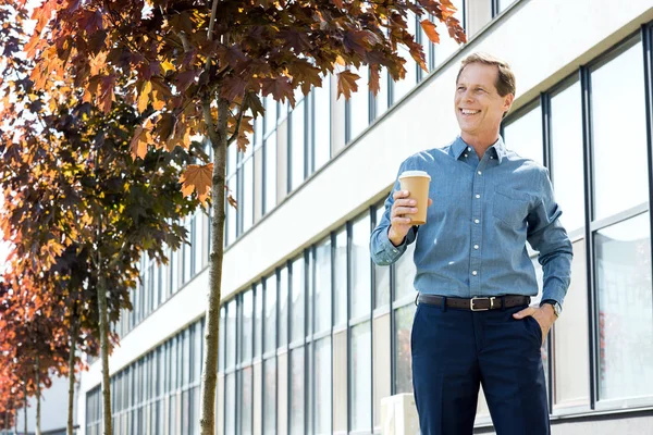 Усміхнений бізнесмен стоїть з кавою, щоб підійти до офісної будівлі — стокове фото