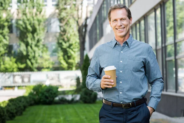 Smiling middle aged businessman standing with disposable cup of coffee near office building — Stock Photo