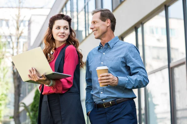 Beautiful businesswoman with laptop and mature businessman with disposable cup of coffee — Stock Photo