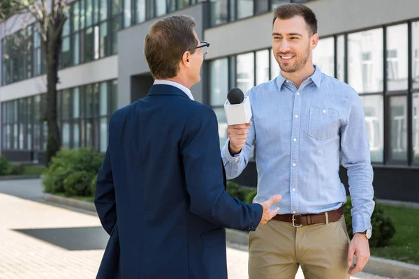 Journaliste souriant professionnel interviewant avec succès homme d'affaires mature avec microphone — Photo de stock