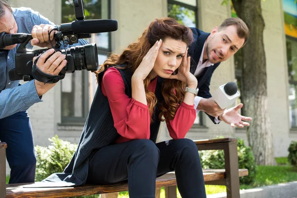 Camarógrafo y presentador de noticias masculino con micrófono hablando con la mujer de negocios frustrada - foto de stock